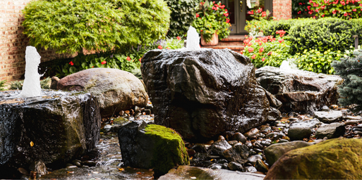 A closeup view of boulder bubblers in front of a home surrounded by summer perennials and shrubs