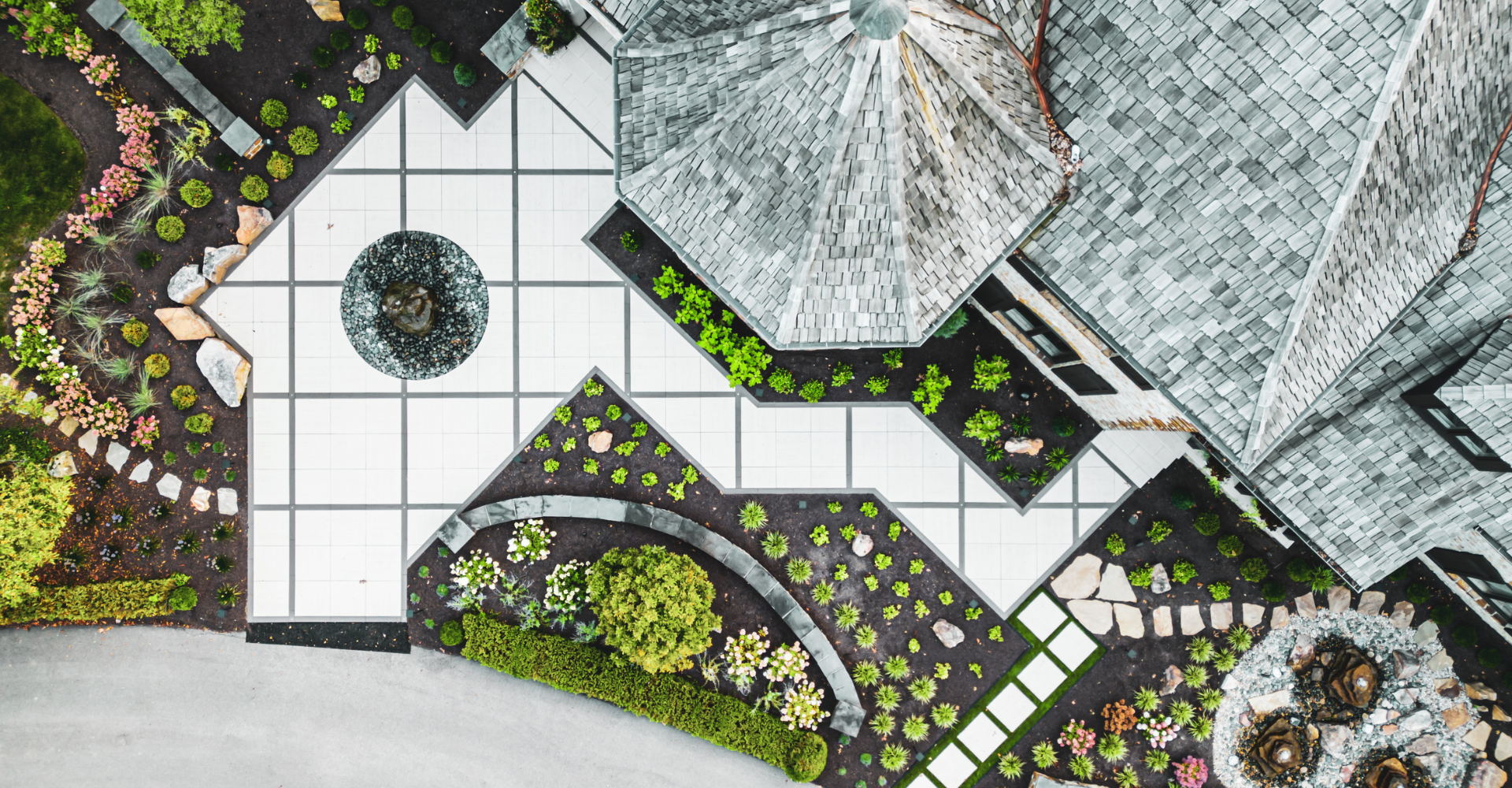 An aerial view of a finished design build project featuring a front yard paver walkway with a rock bubbler in the center and surrounded by softscaping
