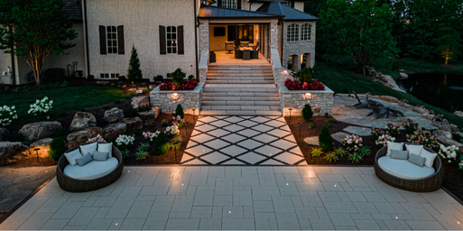 Aerial night view of a paver staircase that leads to a pathway lined with softscaping and embedded with landscape lighting