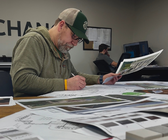 A Wasson landscape designer pouring over project plans with a pencil and sketch in-hand at a table.