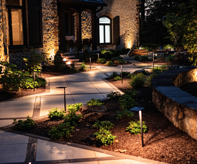 Night view of a front paver walkway with landscape lighting and softscaping