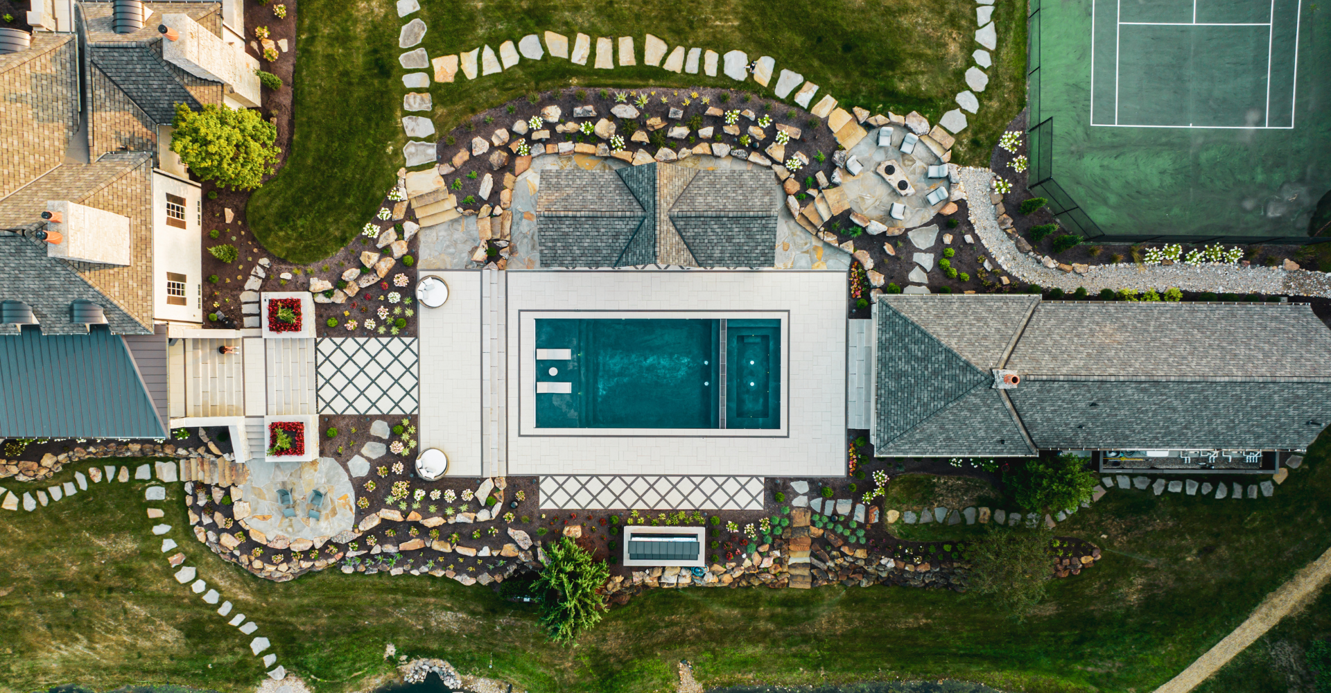 An aerial view of a finished design build project featuring a pool, pergola, patio, pavers, firepit, and softscaping