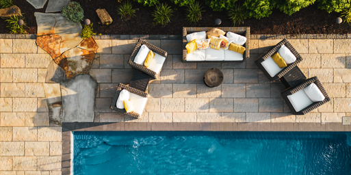 Aerial view of outdoor living patio furniture next to a pool and sitting on a paved patio with a natural stone pathway