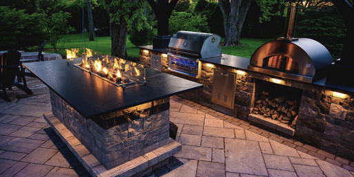 An outdoor kitchen featuring a fireplace-island and full kitchen appliances under a pergola