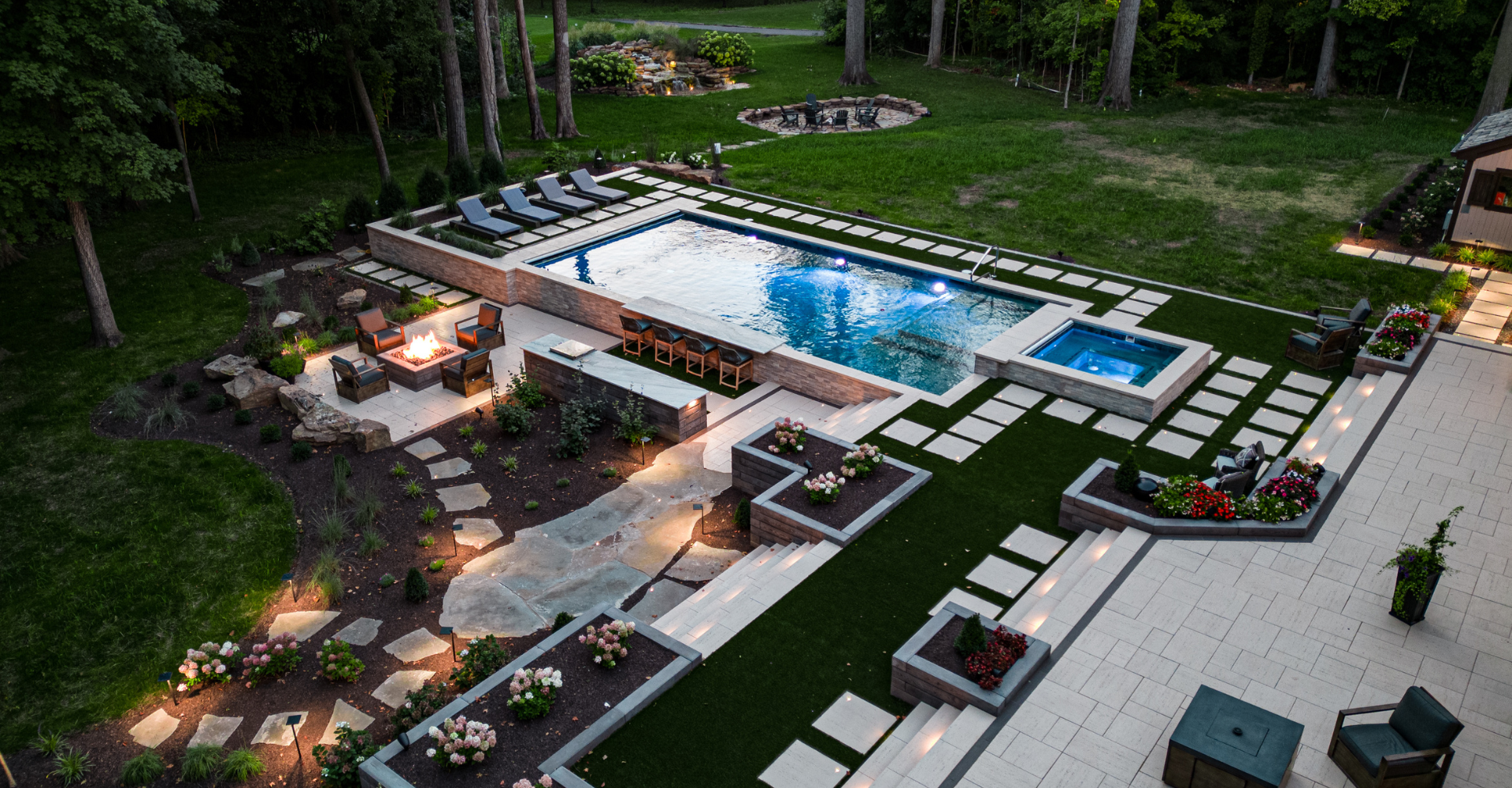 Aerial view of a full design build including a pool, patio, teraced turf, outdoor kitchen, firepit, and hot tub