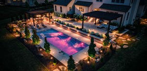 Landscape design with smart lighting and a color-changing, lit in-ground pool surrounded by softscaped trees and perennials.
